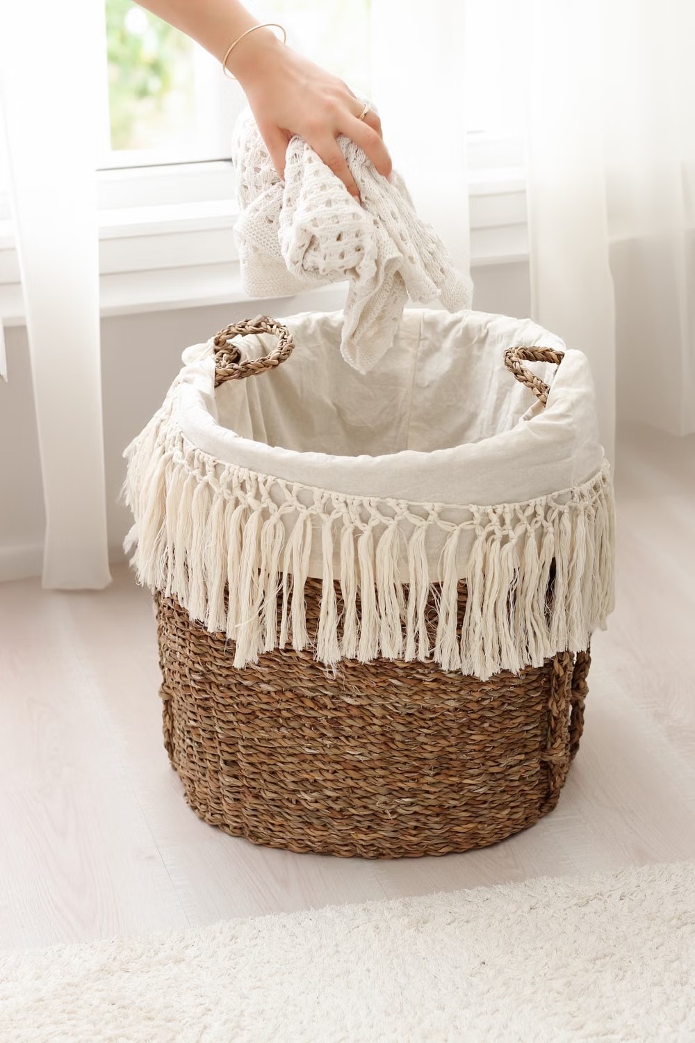 Stock photo of a hand placing a light household textile in a woven laundry basket.
