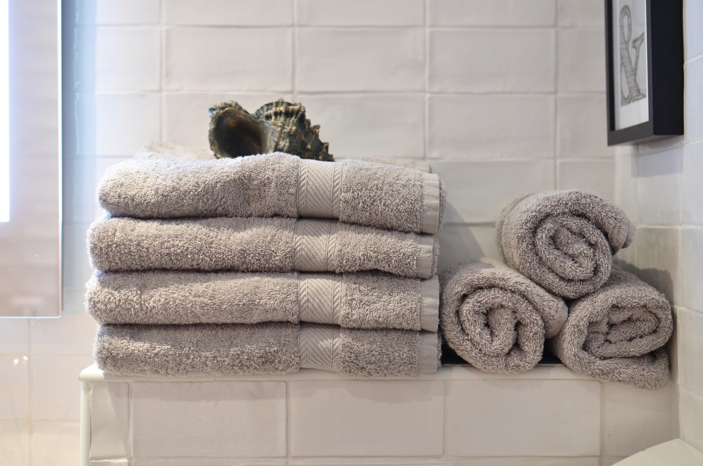 Stock photo of folded and rolled gray towels on a bathroom shelf.